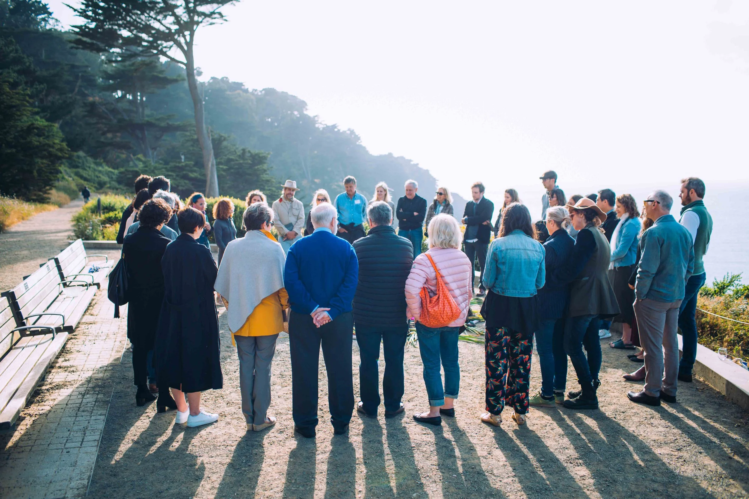 A circle of practitioners gathered together outdoors by the coast at golden hour