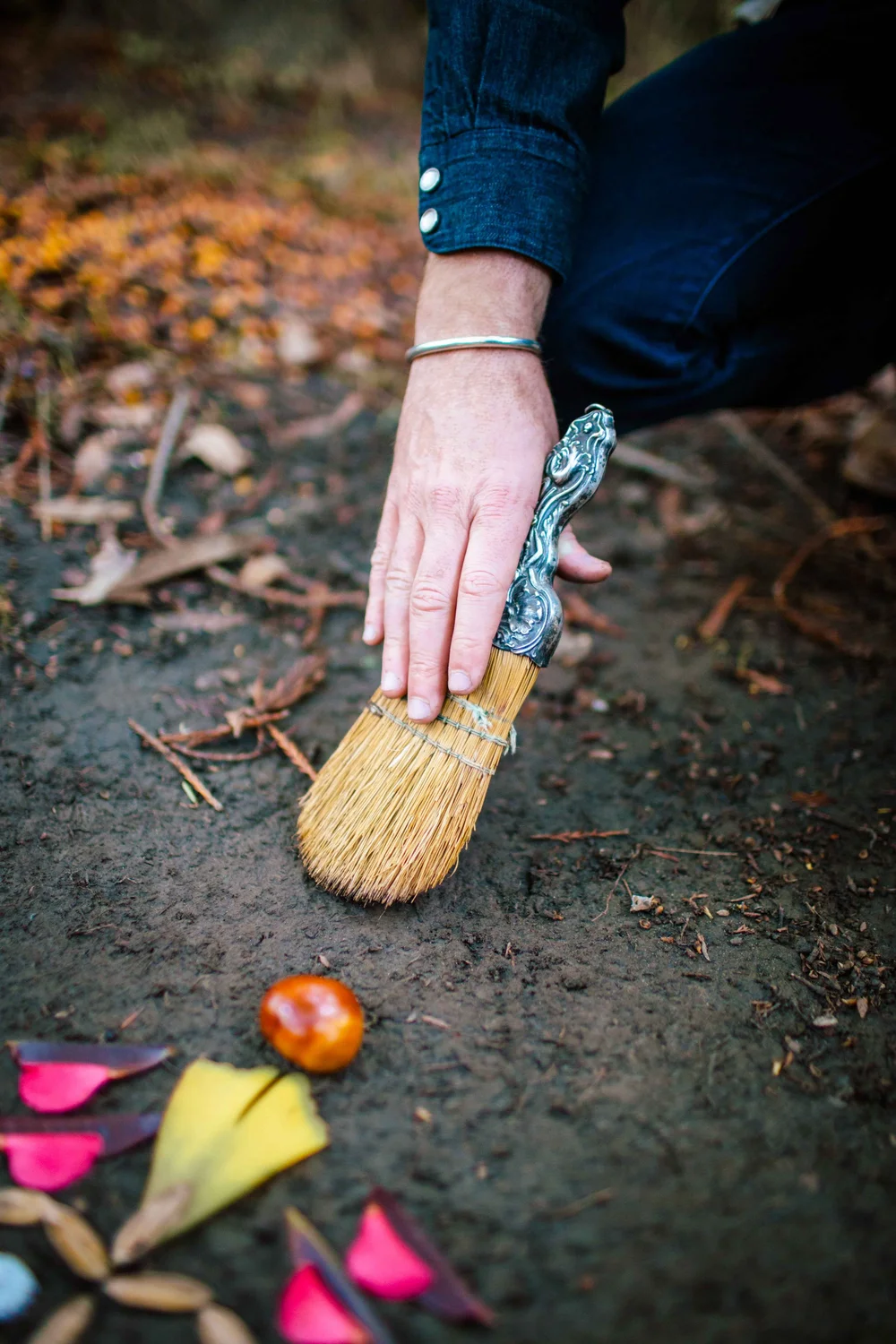 Hands sweeping a small ground space clear with a brush before building an altar
