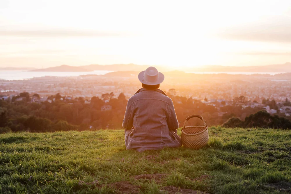 A person sitting on a hilltop at sunrise with a gathering basket